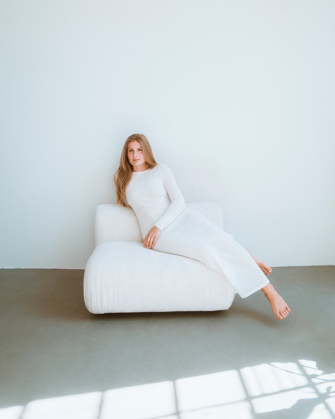 Aleksandra in a light dress on a white armchair, in window light